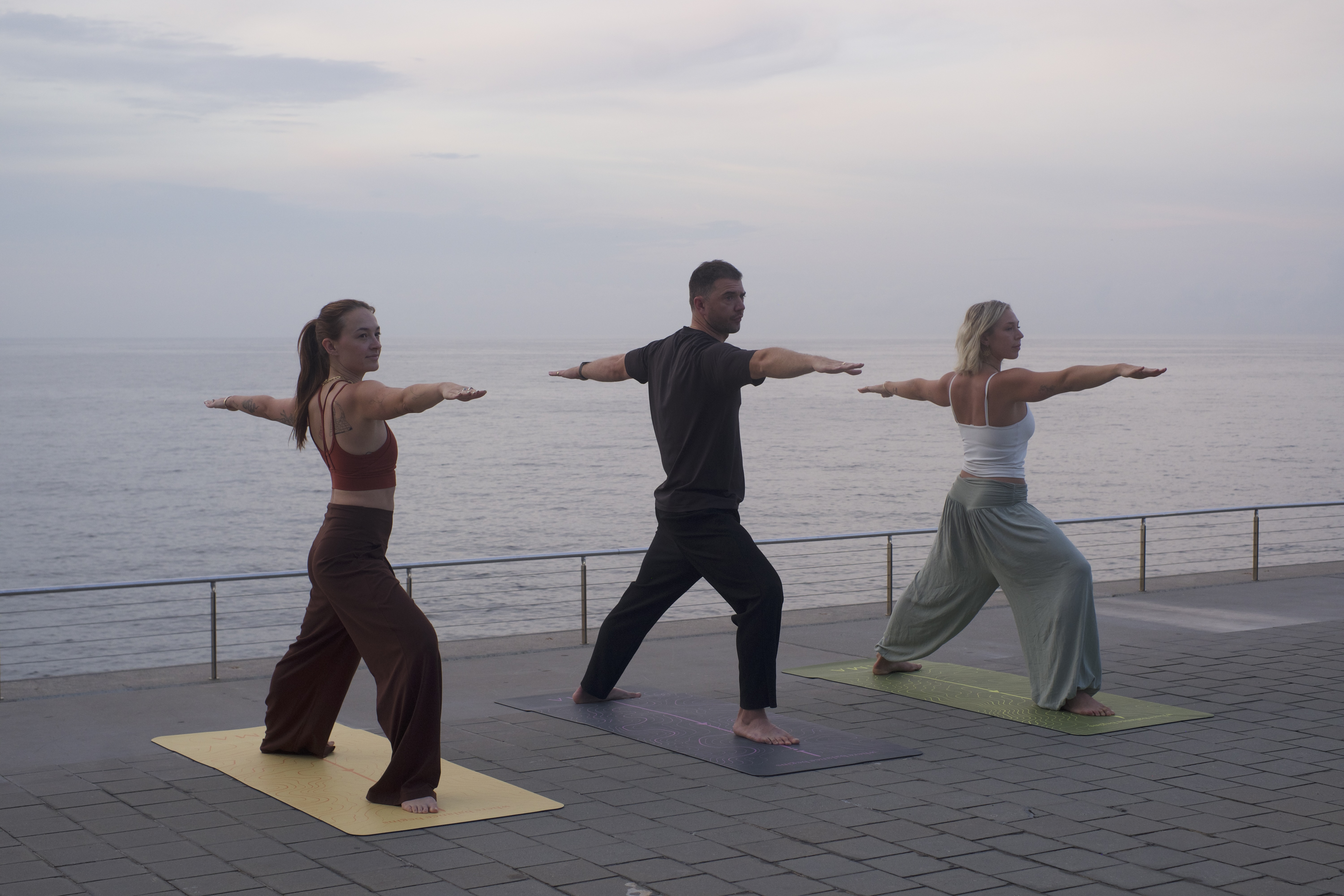 Three people practising warrior pose together by the sea